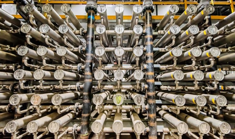 A rack of interconnected large silver tubes and pipes used to house filtration membranes for industrial chemical processing.