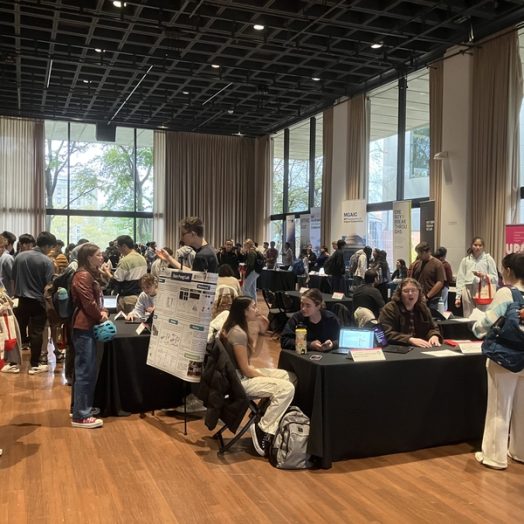Students mill about a large room with numerous staffed tables with black tablecloths.