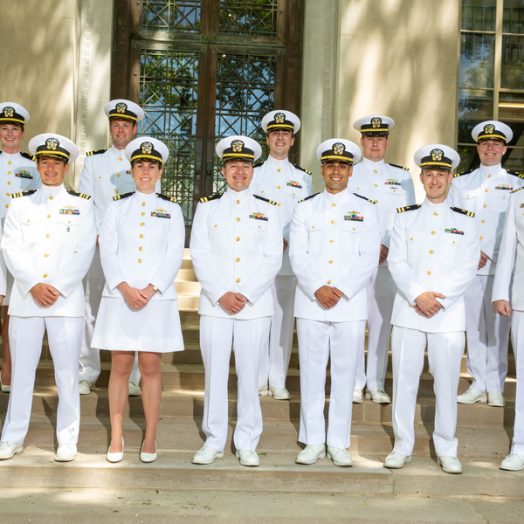 12 naval officers in white uniforms pose together on the MIT campus