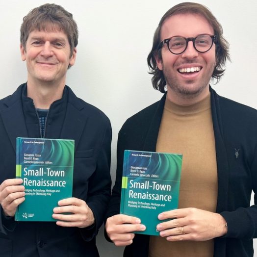 Brent Ryan and Carmelo Ignacolo pose together, each holding up the book “Small Town Renaissance: Bridging Technology, Heritage and Planning in Shrinking Italy.”
