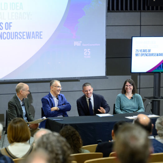 Four people sitting at a table speaking to an audience, with a screen in the background that states, From Bold Idea to Global Legacy: 25 years of MIT OpenCourseWare
