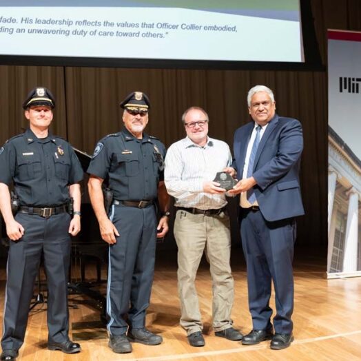 Anantha Chandrakasan presents an award to Michael Grenier, flanked by two MIT police officers in uniform on stage